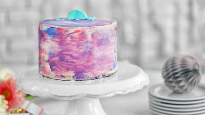 Cake in pink and violet colours on white cake board.