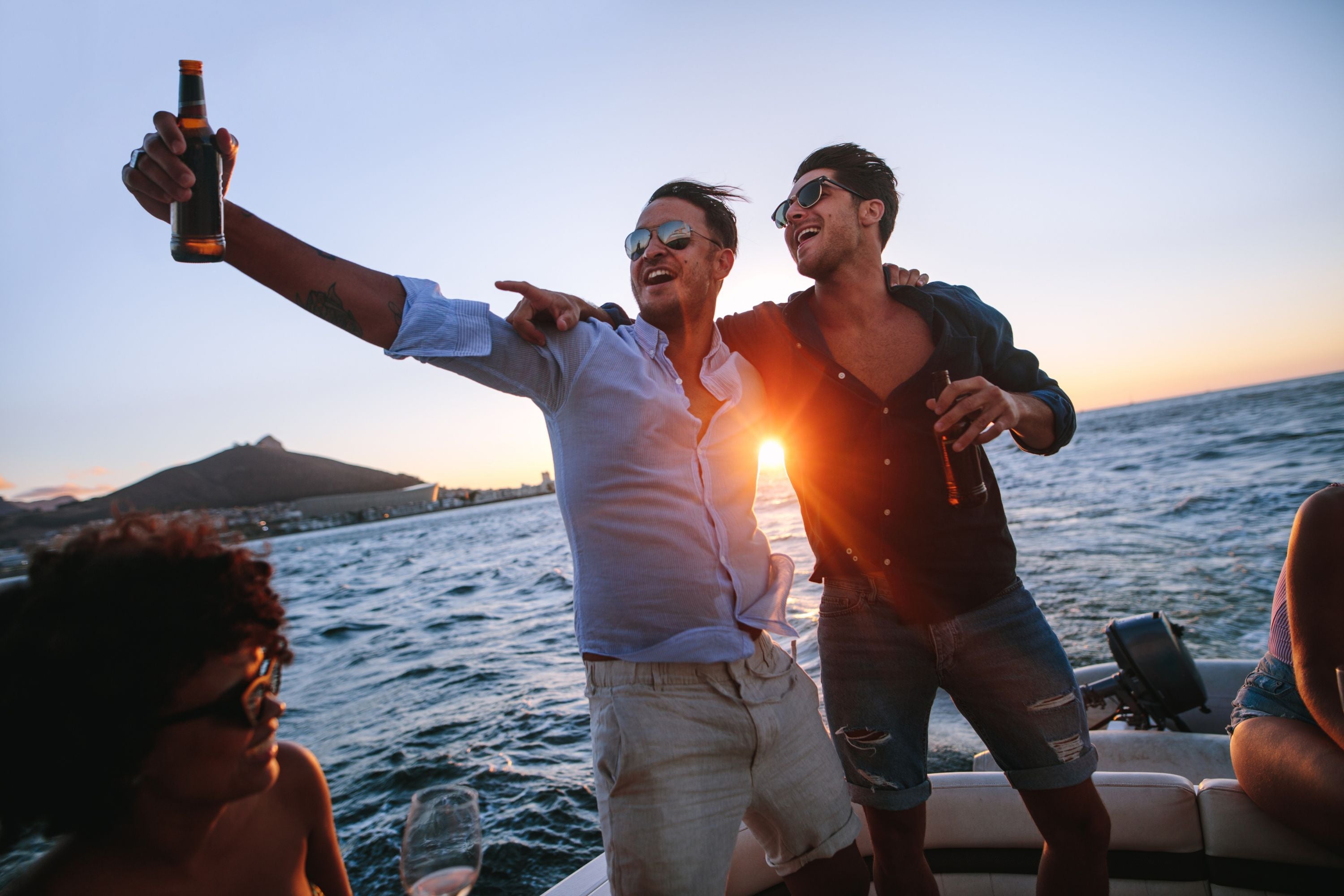 Two mates enjoying drinks on a boat at sunset during a bucks party celebration.