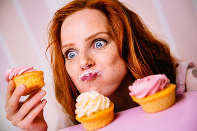Woman playfully eating three different cupcakes.