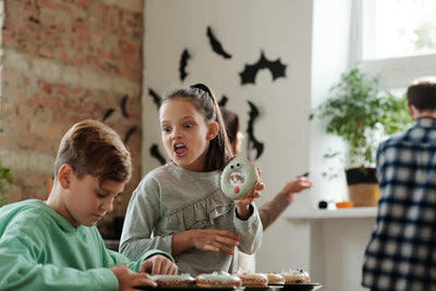 Girl showing to his brother decorated Halloween doughnut.