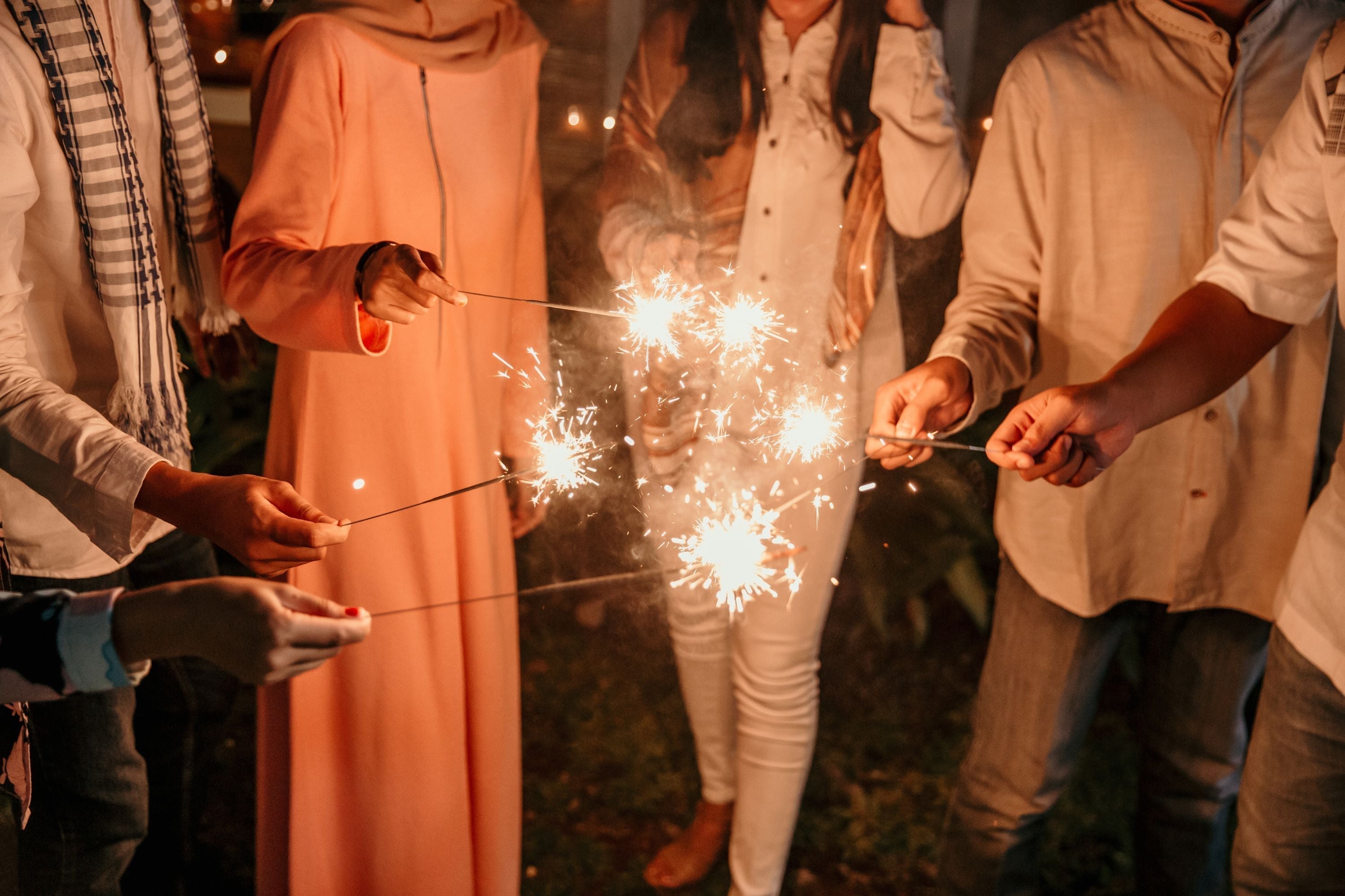 A group of people dressed in traditional and casual clothing holding sparklers during a Eid party celebration.