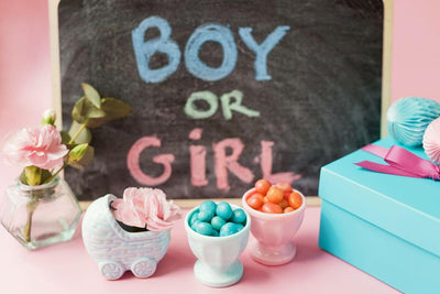 A gender reveal setup with a sign reading "BOY OR GIRL" next to pastel pink and blue decorations and small treats in bowls.